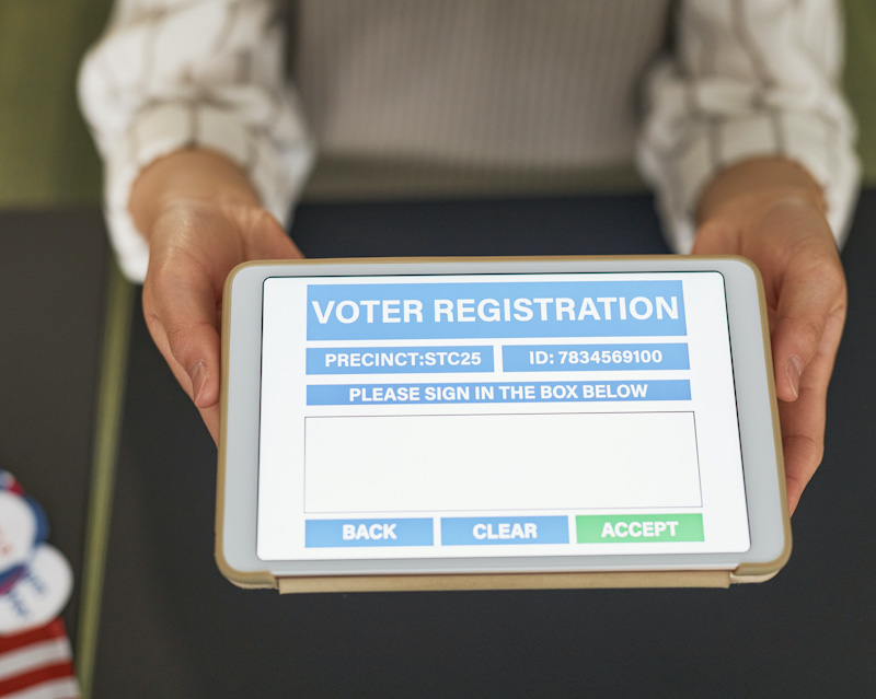 A person holding an electronic device with the words voter registration on it.